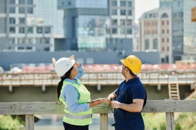 Baustelle Arbeiter Zwei Bauarbeiter auf einer Brücke beobachten etwas im Hintergrund, während sie sich unterhalten.