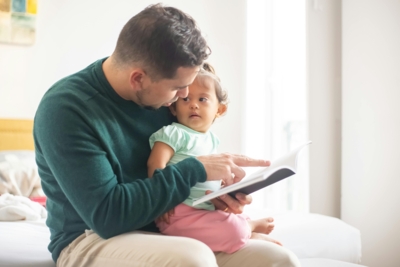 Ein Vater und ein Baby sitzen auf einem Bett und lesen gemeinsam ein Buch.